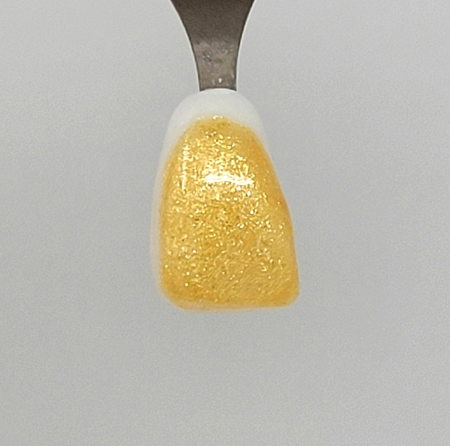 Fine Light Gold Sparkle Temporary Tattooth Colorant on a demo tooth.  These colorants can be applied to teeth to temporarily alter their color or iridescence.